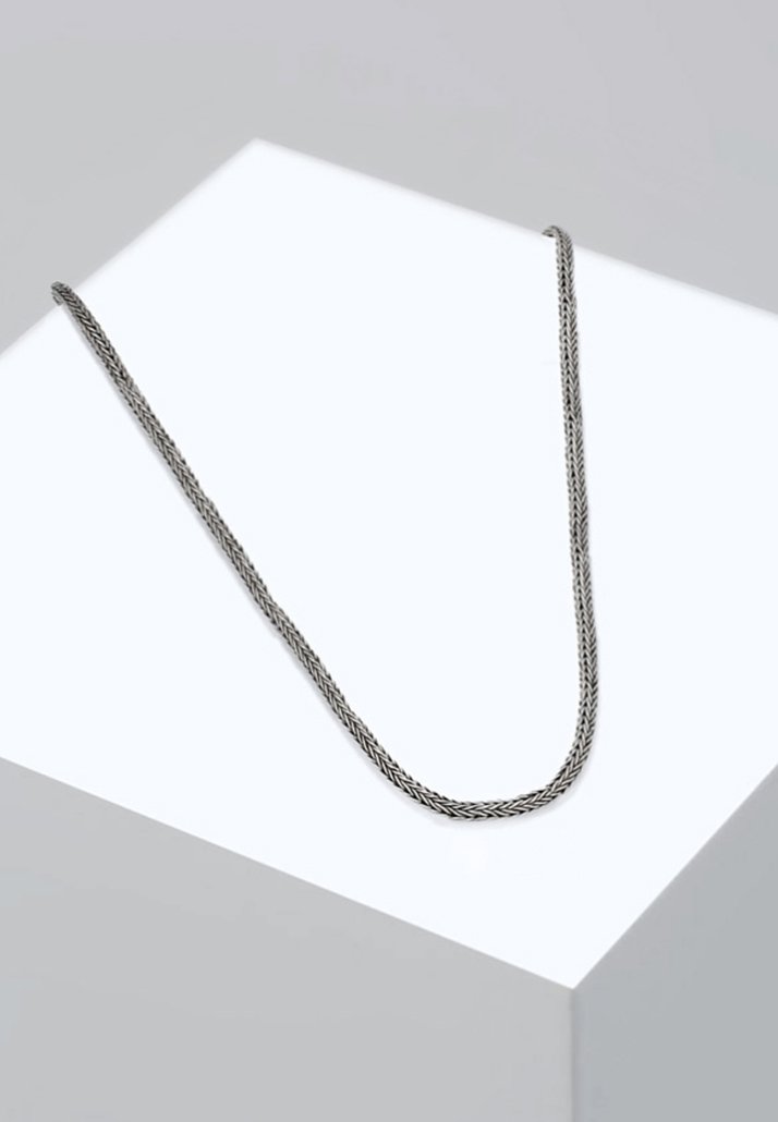 Collana d'argento intrecciata con una texture liscia, esposta su un piedistallo bianco. Il design presenta un sottile motivo a zigzag lungo la sua lunghezza.