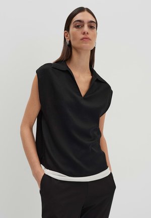 Top sans manches noir avec un col en V, présentant un ourlet inférieur blanc. Fabriqué à partir d'un tissu lisse avec une coupe décontractée.