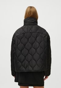 Black quilted puffer jacket with a high collar; features a textured pattern of overlapping shapes, elastic cuffs, and a cropped cut.