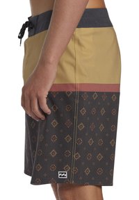 Pantaloni da bagno gialli e grigi con un motivo geometrico su tessuto scuro, con vita regolabile tramite lacci e tasca laterale. Dettagli di cucitura notevoli.