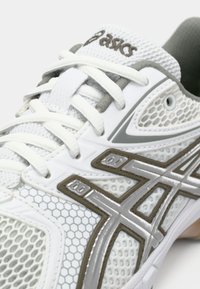 Valge sportlik jalanõu võrgukangast, hallide detailide ja kuusnurkse mustriga. Omab paelu ja polsterdatud keelt lisatoeks.