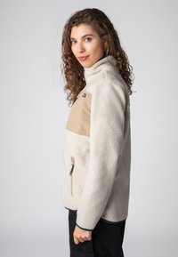 Fleecejacke in Off-White mit einem beigen Brustpanel. Verfügt über eine Reißverschlusstasche und einen hohen Kragen. Weicher Stoff und lässige Passform.