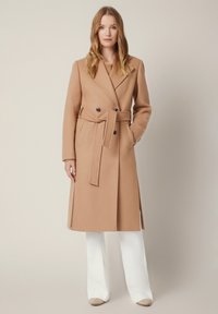 Płaszcz z mieszanki wełny w kolorze camel, z podwójnym zapięciem, szerokimi klapami, paskiem w talii oraz dwoma bocznymi kieszeniami.