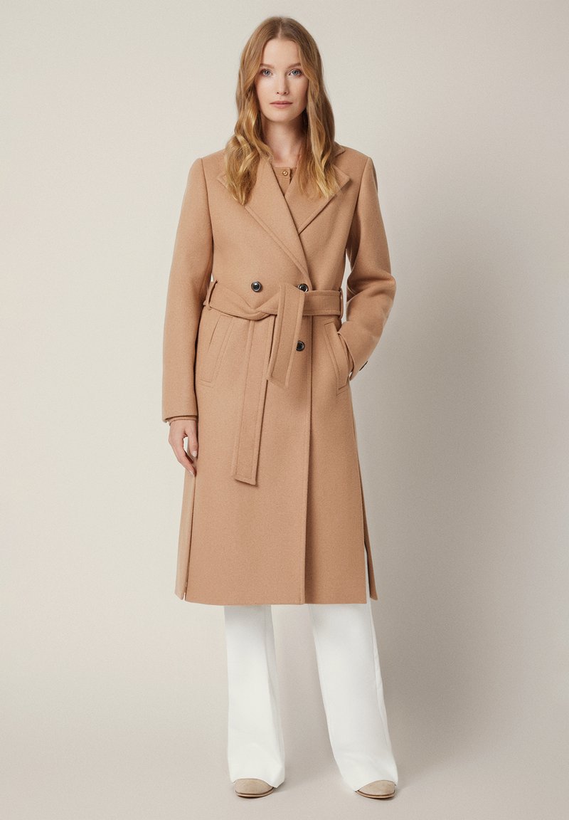 Płaszcz z mieszanki wełny w kolorze camel, z podwójnym zapięciem, szerokimi klapami, paskiem w talii oraz dwoma bocznymi kieszeniami.