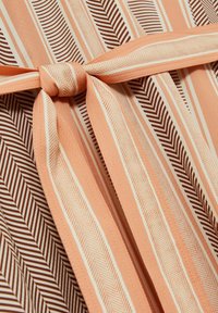 Tkanină pentru rochie cu dungi alternative de piersici și maro, cu un model de herringbone. Fixată cu un centură de culoare piersică, având o textură netedă.