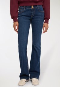 Granatowe dżinsy w fasonie dzwonów o gładkiej fakturze, z dwoma złotymi guzikami w pasie i zaokrąglonymi kieszeniami z przodu.