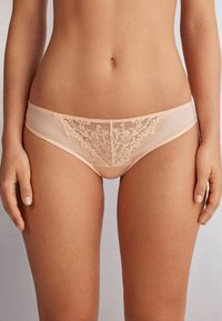 Nude kleurige lingerie met een doorschijnende stof en delicate bloemenkant details aan de voorkant, met gladde randen en een comfortabele pasvorm.