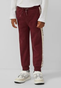 Burgunderfarbene Jogginghosen mit elastischem Bund, Kordelzug und cremefarbenen Seitestreifen mit Text. Weicher Stoff mit schmaler Passform.
