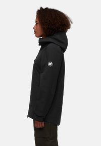 Svart huva jacka med slät yta, dragkedja fram och logotyp på ärmen. Har en avslappnad passform och justerbar dragsko på huvan.