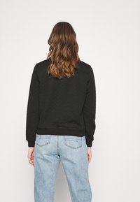 Sweat-shirt noir matelassé avec un col rond, des poignets et un ourlet côtelés, porté avec un jean bleu clair taille haute, vu de dos.
