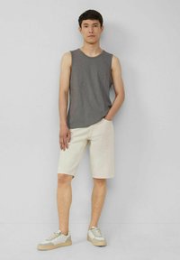 Männer grau ärmelloses Hemd und beige Shorts, kombiniert mit hellen Sneakers. Das Outfit hat eine klassische Passform und einen lässigen Stil.