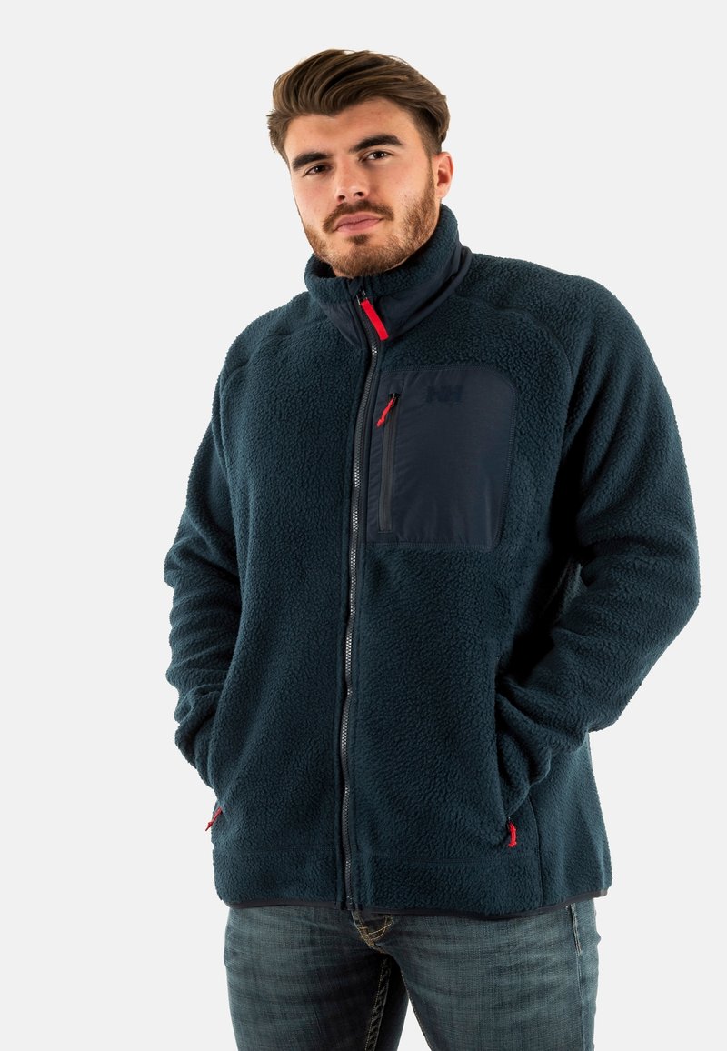 Giacca in pile blu navy con colletto alto, chiusura con zip e tasca sul petto; presenta dettagli rossi e un tessuto morbido e texturizzato.