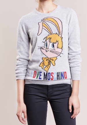 Osoba ubrana w jasnoszary sweter z nadrukiem zająca z kreskówki oraz napisem "LOVE MOSCHINO" w kolorowych literach na dole, w połączeniu z ciemnymi spodniami.
