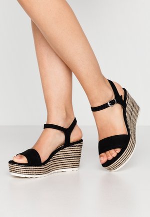 Schwarze Wildleder-Wedge-Sandalen mit einer geflochtenen Jute-Plattform, ausgestattet mit zwei verstellbaren Knöchelriemen und einem offenen Zehendesign.