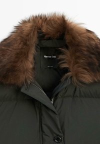Zwarte gewatteerde jas met bruine imitatiebontkraag en zichtbare "Massimo Dutti"-label aan de binnenkant van de halslijn.