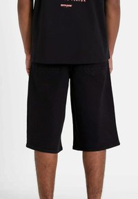 Pantalones cortos de mezclilla negra con un corte holgado, de longitud media hasta el muslo, diseño de cinco bolsillos y detalles de costura sutiles. Tejido liso y texturizado.