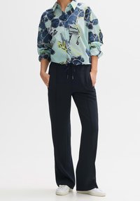 Floral-patterned, light blue collared shirt with rolled sleeves paired with navy pants featuring an elastic waistband and drawstring.