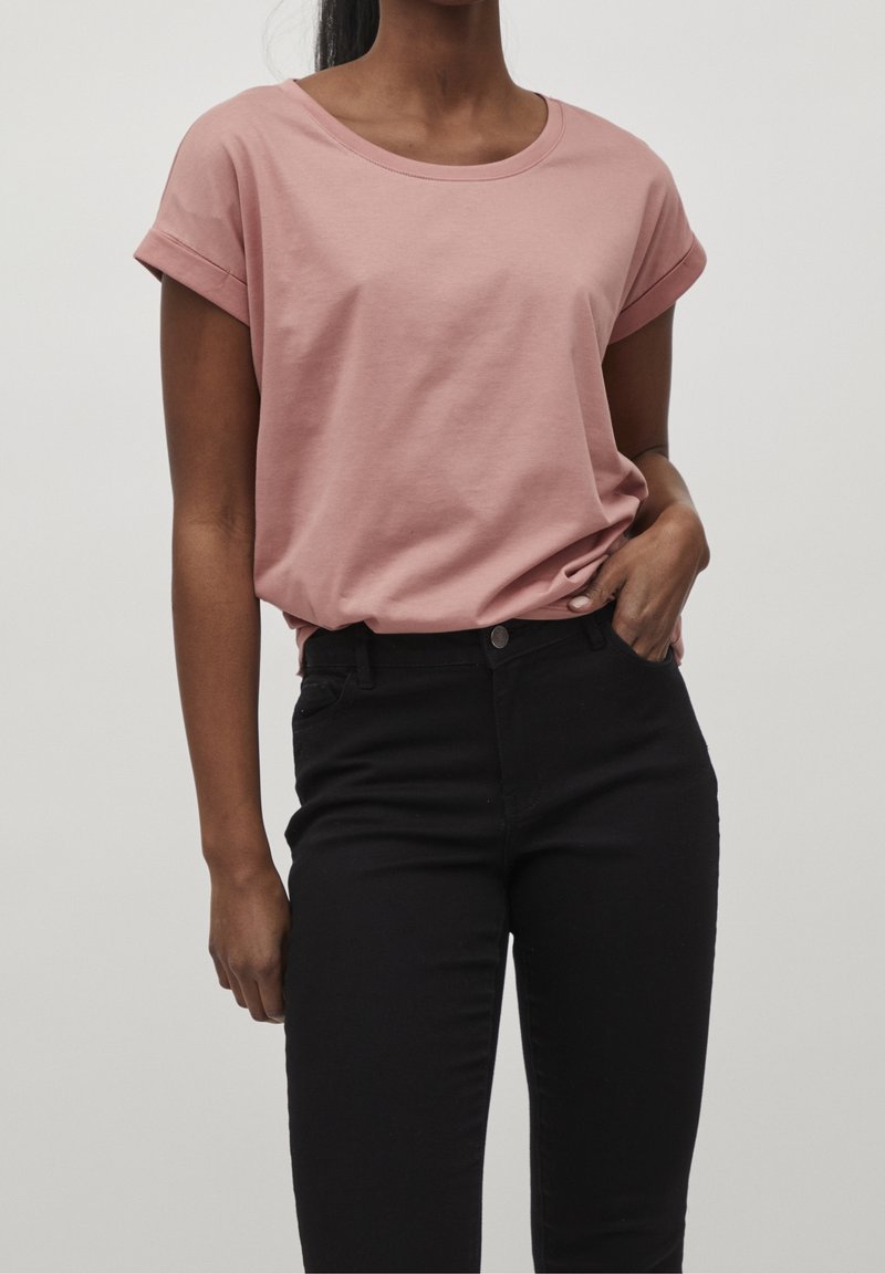 Light pink, short-sleeve cotton t-shirt with a round neckline, paired with black fitted jeans. Shirt has rolled cuffs and a relaxed fit.