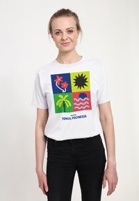 Hvid bomulds T-shirt med et farverigt grafisk design bestående af fire firkanter, der viser blomster, sol, bølger og palmetræer, mærket "Tonga, Polynesien."