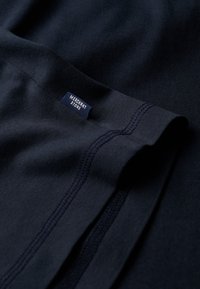 Marineblåt bomuldsstof med glat tekstur, der har et synligt mærke, der læser "MERCHANT STORE" og rene syningsdetaljer.