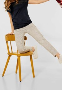 Námořnická blůza s krajkovými detaily, světle béžové slim-fit džíny a bílé tenisky, sedící na jasně žluté dřevěné židli.