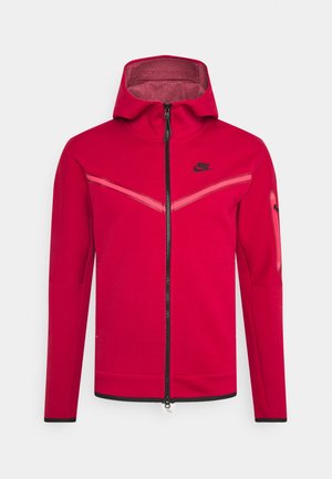 Chaqueta roja con cremallera y capucha, con detalles en negro y un acabado texturizado. Incluye patrones en forma de chevron y el logo de Nike en el pecho.