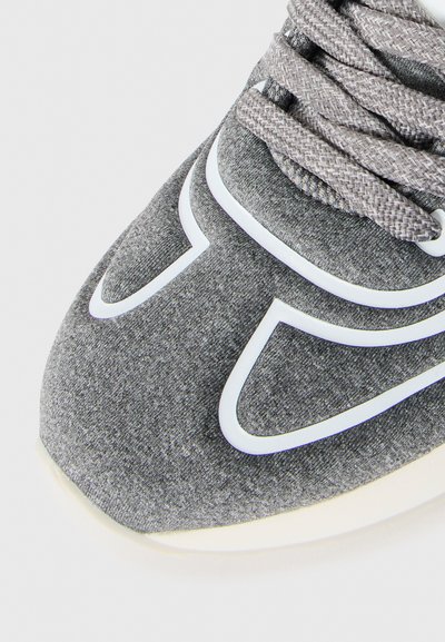 Close-up of gray sneaker toe with textured fabric, white outlined design, and matching gray woven laces.