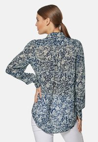 Bluse mit floralem Druck in Marineblau und Hellblau, mit hohem Hals, langen Ärmeln und einem fließenden, leicht durchsichtigen Stoff mit einem gebogenen Saum.
