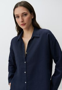Camicia di lino blu navy con colletto, apertura frontale con bottoni e maniche lunghe. Presenta una vestibilità rilassata e una texture morbida.