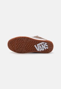 Hnědé nubukové tenisky s gumovou podrážkou. Mají bílé logo Vans, texturovaný protiskluzový vzor a zaoblenou špičku pro aerodynamický tvar.