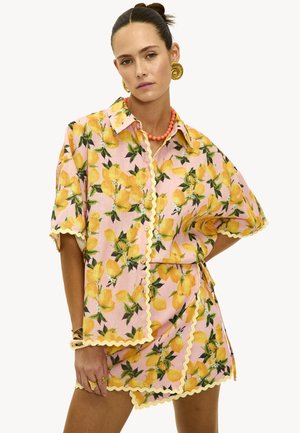 Ensemble floral deux pièces comprenant une chemise à boutons à manches courtes et une jupe assortie. Tissu rose avec un imprimé citron et une bordure jaune à volants.
