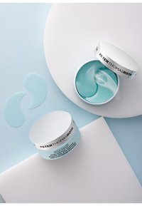 Ein hellblauer Behälter mit einem weißen Deckel, der mit "Peter Thomas Roth" beschriftet ist, enthält Gel-Augenpflaster. Zwei Pflaster sind auf einem hellen Hintergrund platziert.