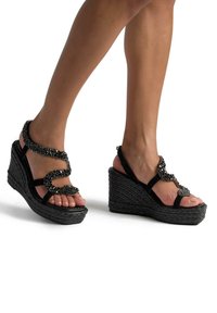 Sandali con zeppa nera e suola intrecciata testurizzata. Presentano una fascia decorativa con perline nere e fasce lisce che assicurano il piede.