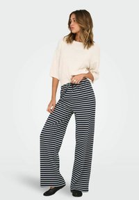 Kremowa, prążkowana bluzka z krótkim rękawem połączona z granatowymi i białymi spodniami w paski o szerokich nogawkach. Spodnie mają elastyczny pas i sznurek do regulacji.