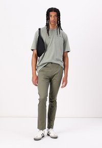 T-shirt en coton vert clair, pantalon vert olive et sac bandoulière noir. Baskets blanches et noires avec des rayures. Coupe droite.