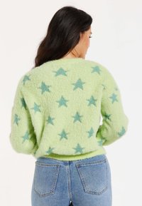 Light green fuzzy sweater with teal star patterns, ribbed hem, and long sleeves, styled with high-waisted blue jeans.