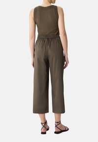 Oliwkowy bezrękawnik z teksturowanymi detalami na ramionach, połączony z lekkimi, luźnymi, khaki spodniami cropped oraz czarnymi sandałami na paski.