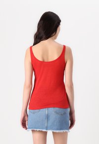Débardeur rouge au design ajusté avec des bretelles larges, associé à une jupe en jean bleu clair avec un ourlet effiloché et des poches arrière.