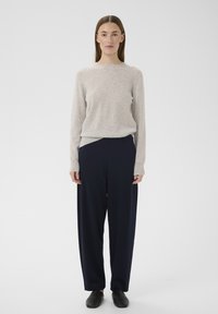 Lysegrå striktrøje, løs pasform, rund halsudskæring; kombineret med sorte, løse bukser med højtaljet pasform; sorte, ensfarvede slip-on sko.