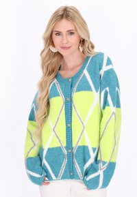 Lehký, oversized cardigan v barvě teal a neonově zelené s bílými diamantovými vzory. Obsahuje žebrovaný límec a zlaté zapínání na knoflíky.