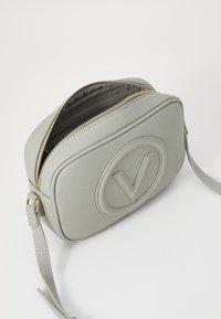 Γκρι δερμάτινη τσάντα ώμου με υφασμάτινη επιφάνεια, οβάλ λογότυπο, χρυσό φερμουάρ και ρυθμιζόμενο λουρί; διαθέτει ορθογώνιο σχήμα και εσωτερικές θήκες.