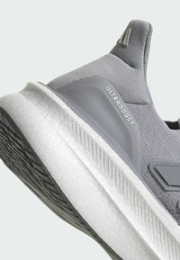Sive mrežaste atletske tenisice s teksturiranim gornjim dijelom, ULTRABOOST brendiranjem i bijelim jastučićem na potplatu koji ima uzorčeni crni donji dio.
