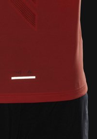 Rød kortærmet sports T-shirt med et struktureret mønster, refleksstribe og logo nær kanten, parret med mørke shorts.