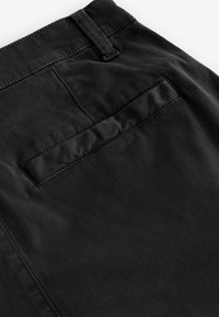 Pantalones de algodón negros con una textura suave, que cuentan con un bolsillo trasero con solapa cosida y trabillas a lo largo de la cintura.