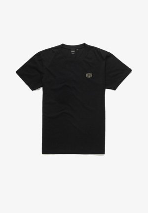 Camiseta de algodón negra con mangas cortas y cuello redondo. Presenta un pequeño logotipo circular dorado en la parte izquierda del pecho.