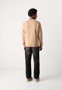 Sweatshirt beige à manches longues et ourlet côtelé, associé à un pantalon en denim foncé et des chaussures de couleur claire, présenté de dos.
