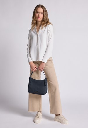Navy handbag with a textured finish, stylish handle, and logo detail. Paired with a white button-up shirt and beige wide-leg pants.