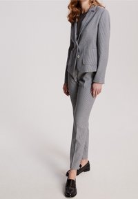 Costume gris à carreaux avec un blazer ajusté et un pantalon slim, fabriqué dans un tissu texturé. Associé à des mocassins noirs pour un look soigné.