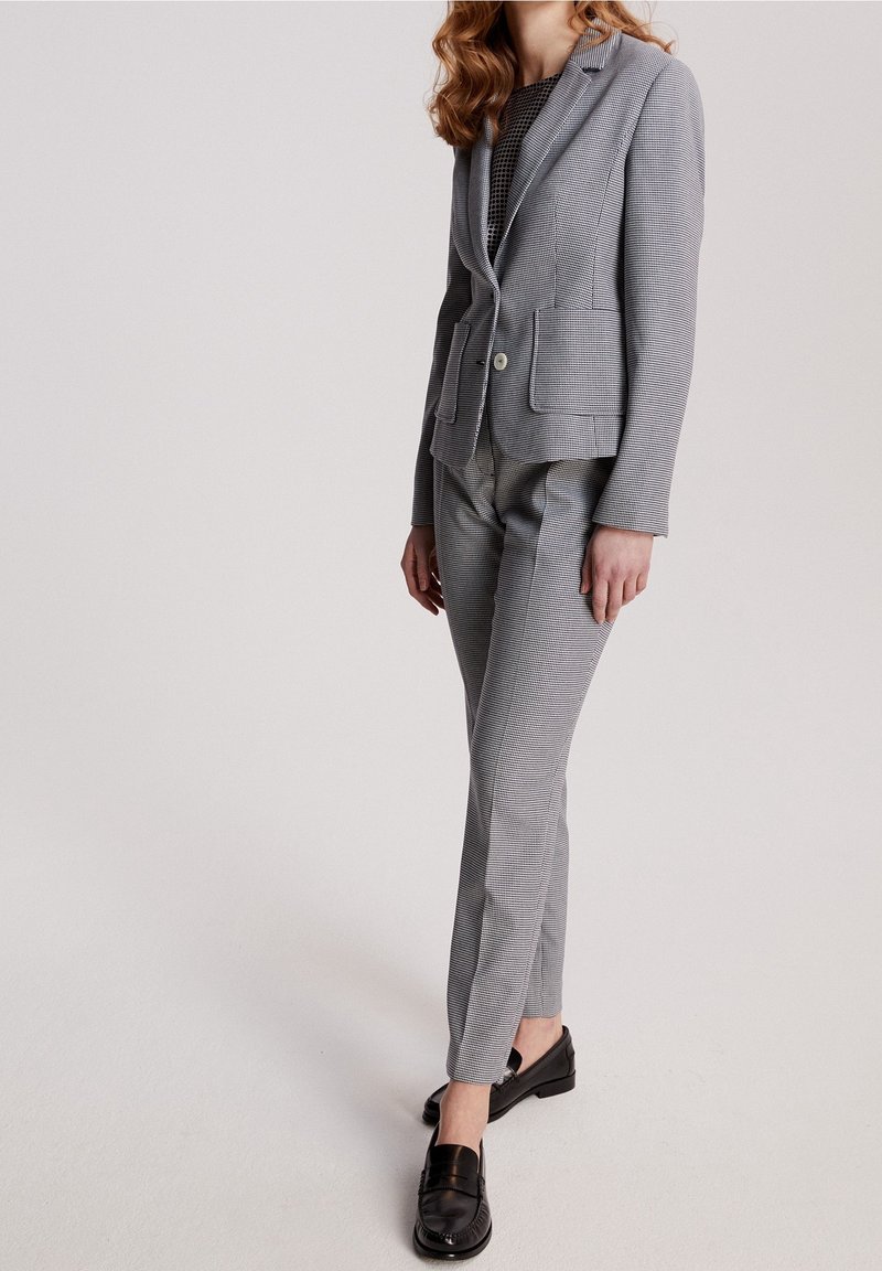 Costume gris à carreaux avec un blazer ajusté et un pantalon slim, fabriqué dans un tissu texturé. Associé à des mocassins noirs pour un look soigné.