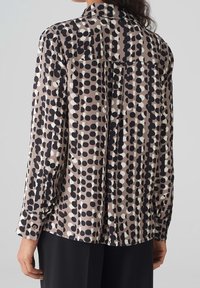 Long-sleeve blouse in a lightweight fabric featuring a geometric pattern of black, white, and beige dots. Includes a buttoned cuff and collar.